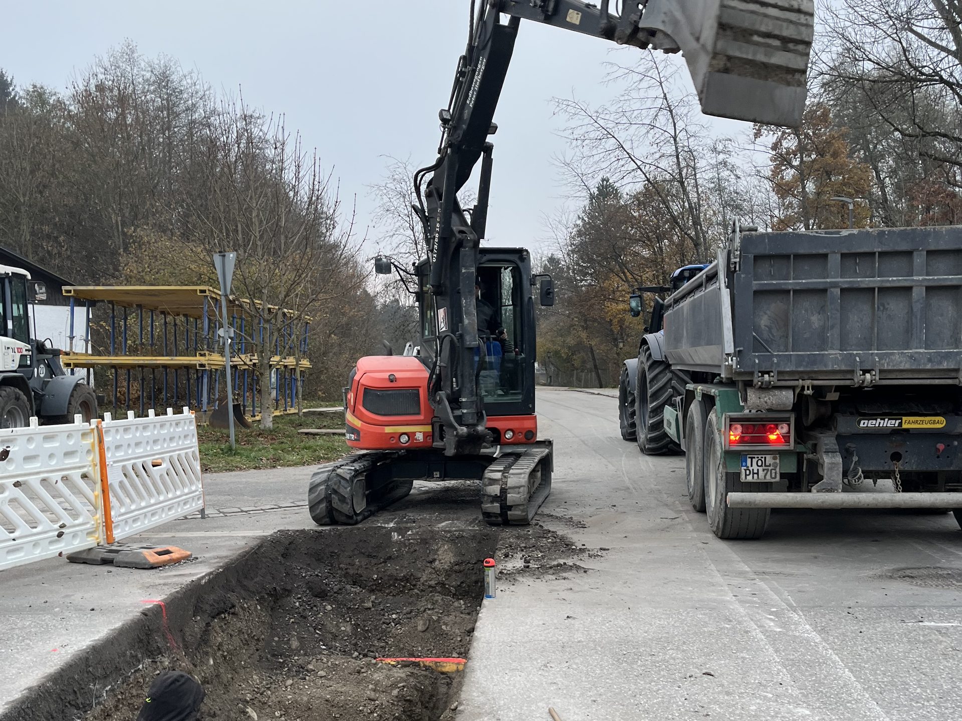 Bagger belädt einen Lkw neben einem offenen Leitungsgraben