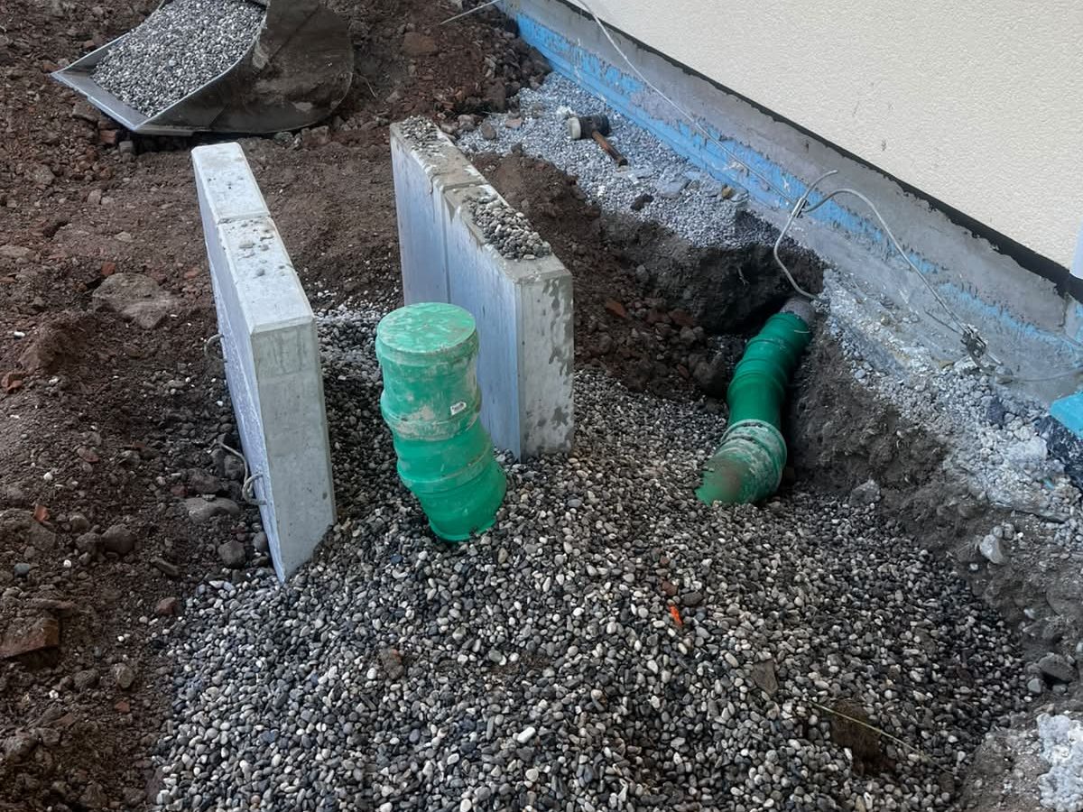 Drainageschacht mit Anschlussrohren an einer Hauswand