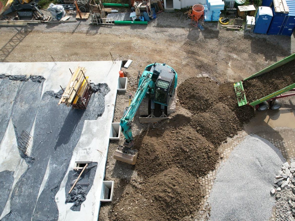 Bagger verteilt Aushub auf einer Baustelle, Luftaufnahme