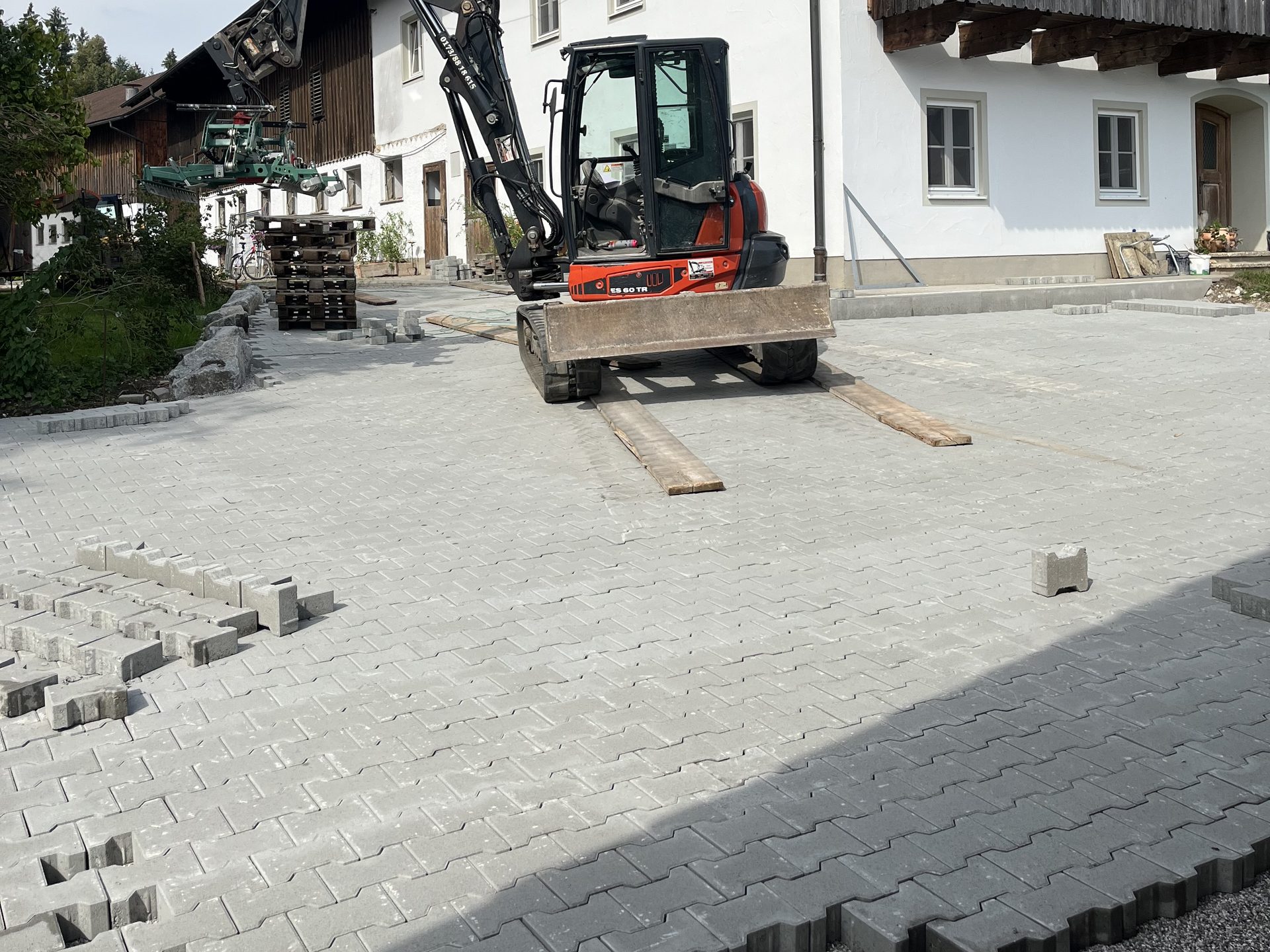 Bagger beim Verlegen einer großen Pflasterfläche vor einem Bauernhaus
